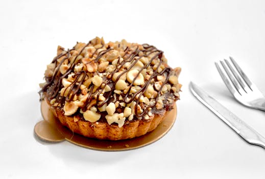Gâteau praliné noisette sur un support doré, garni de morceaux de noisettes et de chocolat fondu.