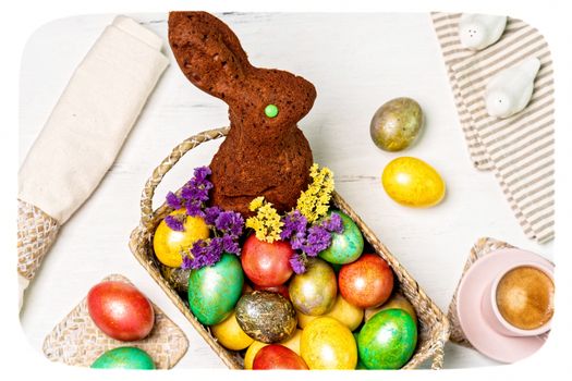 Gâteau en forme de lapin entouré d'œufs colorés et de fleurs dans un panier, décor pour Pâques.