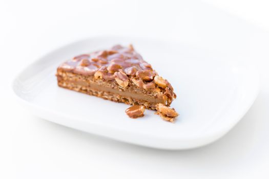Part de gâteau praliné noisette avec une couche croustillante et des morceaux de noisettes sur une assiette blanche.