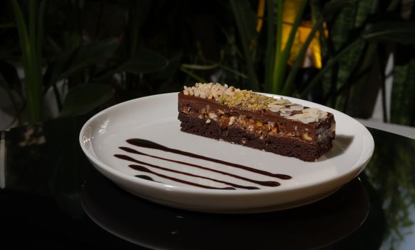 Gâteau praliné noisette sur une assiette blanche, décoré de chocolat et de morceaux de noisettes.
