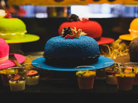 Gâteau bleu décoré de fleurs et fruits, entouré de pâtisseries colorées dans une vitrine.