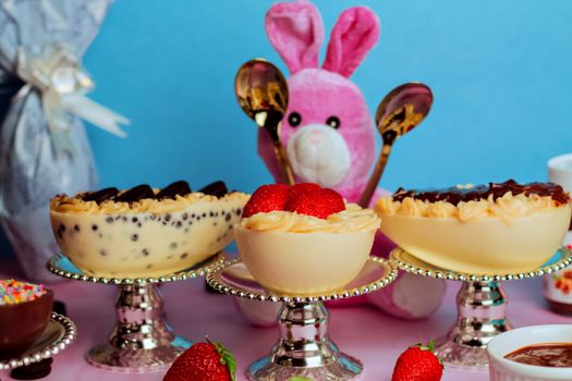 Gâteaux de Pâques décorés de fraises, avec un lapin en peluche et des couverts dorés en arrière-plan.